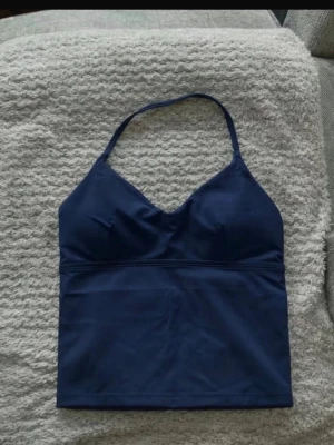 Mörkblå halterneck linnetopp - Snygg mörkblå linnetopp med halterneck och v-ringning. Toppen är ärmlös och har en tight passform som framhäver figuren. Perfekt att träna i. Finns ingen logo