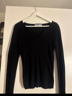 Svart ribbad tröja med v-ringning - Snygg svart ribbad tröja från NA-KD med djup v-ringning och långa ärmar. Tröjan har en figurnära passform och är tillverkad i ett stretchigt material som sitter skönt på kroppen. Perfekt att styla med jeans eller kjol.