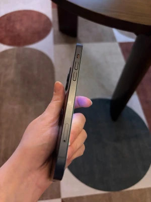 Svart iPhone 12 128GB - Snygg svart iPhone 12 128GB med platt ram i metall och tydliga volymknappar på sidan. Klassisk Apple-design med stilren och modern känsla. Perfekt för dig som gillar en tunn och elegant mobil med premiumkänsla.