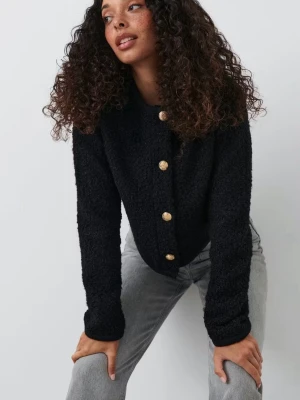 Svart kofta med guldknappar - Stilren svart kofta i teddy-liknande material med rund halsringning och fyra dekorativa guldknappar framtill. Koftan har lång ärm och en rak passform som passar perfekt till jeans eller kjol. Säljer då den inte används 