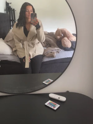 Beige kappa med knytskärp - Snygg beige kappa med bred krage och knytskärp i midjan. Kappan har en avslappnad passform och är perfekt för dig som gillar stilrena och trendiga plagg. Materialet ser ut att vara mjukt och bekvämt, perfekt för kyligare dagar.