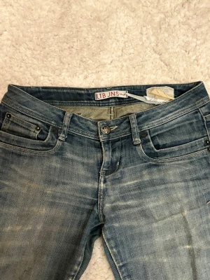 Blå jeans från LTB JNS med slitning - Säljer ett par blå jeans från LTB JNS med snygg slitning och ett litet hål på ena benet. Jeansen har klassisk femficksmodell, låg midja och botcut. Dom är lite slitna i rumpan men har lagat dom så att de går att använda som vanligt! Midjemåttet rakt över är 40 cm och innerbenet är 80 cm