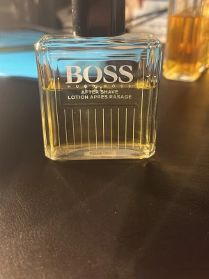 Hugo Boss After Shave Lotion - Stilren after shave lotion från Hugo Boss i en genomskinlig, rektangulär glasflaska med svart lock. Vätskan är ljusgul och flaskan har tydliga vita linjer och logga på framsidan. Perfekt för dig som gillar klassisk och fräsch doft.