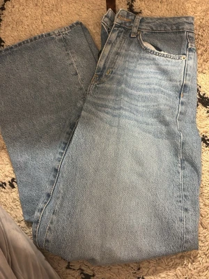 Ljusblå raka jeans vintage-look baggy - Säljer ett par ljusblå jeans med rak passform och klassisk femficksdesign. Jeansen har en snygg vintage-tvätt och slitna detaljer längs bensluten för en avslappnad vibe. Tillverkade i kraftig denim, perfekta för dig som gillar retrostil. Täcken på avvändning