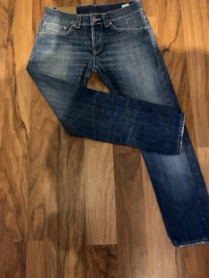 DonDup - Säljer ett par blå jeans med snyggt slitna detaljer och raka ben. Jeansen har klassisk femficksdesign och kontrastsömmar. Perfekta för en avslappnad och trendig look. Materialet är denim i bomull. W30