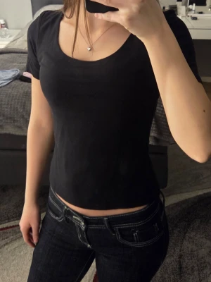 Svart topp med djup urringning Bik Bok - En enkel och stilren svart topp från Bik Bok med korta ärmar och djup, rund urringning. Tillverkad i mjukt bomullsmaterial som sitter skönt och har en normal passform. Perfekt att matcha med jeans eller kjol.