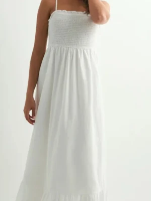 Vit långklänning med smockliv - Luftig vit långklänning med smala axelband och smockat liv. Klänningen har en volangkant nertill och är tillverkad i ett lätt material som passar perfekt för varma dagar. Enkel och stilren design som ger en romantisk känsla.