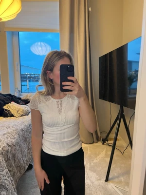 Vit topp med spets från Y.A.S - Supersöt vit topp från Y.A.S med spetsdetaljer vid axlar och halsringning. Topp i ribbad struktur och korta ärmar, perfekt för en fräsch och stilren look. Materialet är mjukt och stretchigt för extra komfort.