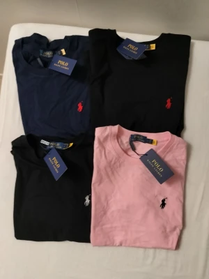 Polo Ralph Lauren t-shirts i flera färger. Alla 4 och en gratis  - Fyra klassiska t-shirts från Polo Ralph Lauren i färgerna marinblå, svart och rosa. Alla har rund halsringning, korta ärmar och den ikoniska broderade loggan på bröstet. Perfekta för en stilren och avslappnad look. 459 per st.