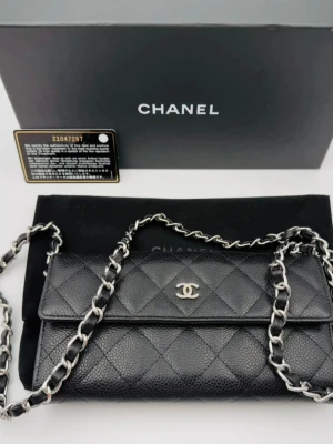 Chanel caviar Wallet on chain - Säljer en klassisk svart axelväska från Chanel i quiltat caviar läder med silverfärgad kedjerem och ikoniska CC-loggan framtill. Väskan har elegant rektangulär form och tidlös design som passar till allt. Perfekt för dig som vill ha en lyxig och stilren accessoar. Äkthetskort, dustbag och box medföljer. Köpt via Vestiaire Collective och är fysiskt autentiserad. 