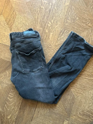 Svarta slim fit jeans - Säljer ett par svarta gant slim fit jeans med klassisk femficksdesign och diskreta slitningar. Jeansen har en svart patch bak i midjan som det står Gant och är sydda i mjukt denimtyg. Kan inte se vad det är för storlek men är nog S. Köpte dom från h&m tror jag👍👍