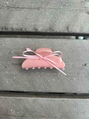 Rosa hårklämma med rosett - Söt ljusrosa hårklämma  med en matchande rosett framtill. Klämman har klassisk form med rundade kanter och små piggar för bra grepp. Perfekt accessoar för att piffa till frisyren med en gullig detalj. Silikon på insidan som bidrar till bättre grepp i håret. Söt, funktionell och hållbar💕