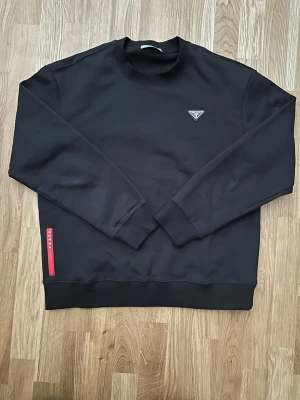 Prada svart sweatshirt - Säljer en stilren sweatshirt i storlek XL från Prada. Tröjan är i mycket bra skick och har bara använts enstaka gånger då den är för liten för mig. Passar också i L. Perfekt basplagg som funkar till det mesta. Priser går att diskuteras