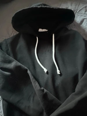Svart hoodie från Pier One - Svart hoodie från Pier One med klassisk design, vit dragsko i huvan och mjukt material. Perfekt för en avslappnad stil och enkel att matcha med jeans eller joggers.