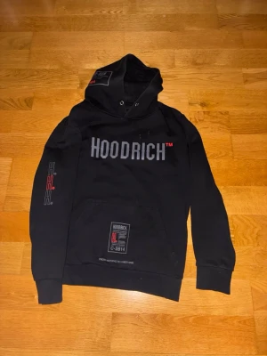 Svart HOODRICH hoodie med tryck - Svart hoodie från HOODRICH med stora tryck både fram och bak. Knappt använd och storlek L.
