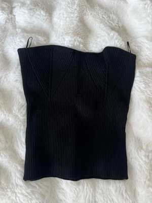Svart ribbad tubtopp från Gina Tricot - Snygg svart ribbad tubtopp från Gina Tricot med  markerade sömmar framtill. Toppen är tight och har en stilren design som passar perfekt till många olika outfits.