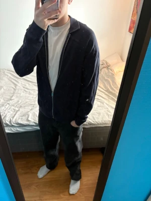 Mörkblå zip tröja - Mörkblå ziptröja med krage och ribbade muddar. Tröjan har en enkel och stilren design, perfekt att bära över en t-shirt. Passar dig som gillar en avslappnad men snygg look.