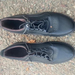 Svarta Timberland sneakers i skinn - Säljer ett par svarta sneakers från Timberland med snygga vita sömmar och rund tå. Skorna har snörning och är tillverkade i skinn med en cool detalj på sulan. Insidan är fodrad i mörkbrunt tyg för extra komfort. Perfekt för dig som gillar stilrena och klassiska sneakers.