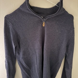 Mörkblå stickad tröja med half zip - Snygg mörkblå stickad tröja med ribbad krage och half zip-dragkedja. Långärmad modell som är perfekt för kyliga dagar. Enkel och stilren design som funkar till många olika looks.