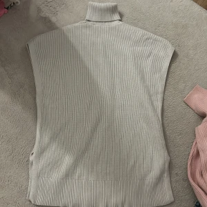 Beige polotröja utan ärmar - Säljer en beige ribbad polotröja utan ärmar. Tröjan har hög krage och är stickad i ett mjukt material, perfekt att styla över en skjorta eller t-shirt. Enkel och clean look som passar till många outfits. Modellen är lämgre och oversize🩷