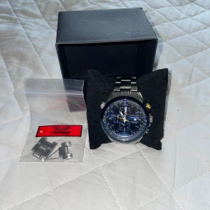 Champion Outlander blå kronografklocka - Snygg kronografklocka från Champion Outlander med blå urtavla, silverfärgat armband i metall och detaljer i gult och vitt. Klockan har datumvisning, flera små urtavlor och robust design. Perfekt accessoar för dig som gillar stilrena och sportiga klockor. OBS Behöver batteribyte