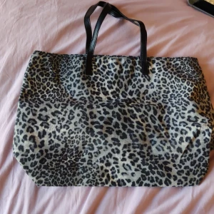 Leopardmönstrad väska - Stor och rymlig shoppingväska med leopardmönster i svart och beige. Väskan har två svarta handtag i skinnimitation och en mjuk, flexibel form som gör den enkel att bära med sig. Perfekt för att få plats med allt du behöver under dagen.knappt andvänd