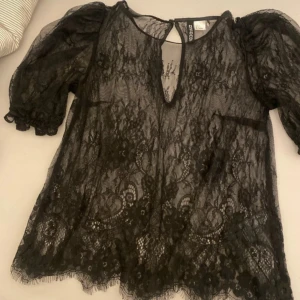 Svart spetsblus från h&m  - Supersnygg svart blus i transparent spets från h&m. Puffiga korta ärmar med rynk vid mudden, v-ringad öppning fram och fina spetsdetaljer över hela toppen. Perfekt för dig som gillar statement-plagg med cool vibe.