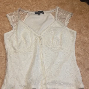 Vit och svart spetsblus från Almost Famous - Två snygga blusar i spets från Almost Famous, en i vit och en i svart. Båda har v-ringad front med knyt, genombrutna spetsärmar och figurnära passform. Från usa men har inte haft nån användning för dom en för 80 båda för 160 men det står shien där under jag vet att jag köpte den från usa dock 
