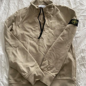 Stone Island junior half zip tröja  - Snygg beige långärmad tröja från Stone Island med svart half zip och klassisk logga på ärmen. Tröjan har hög krage och är gjord i mjuk bomull, perfekt för en chill och stilren look.