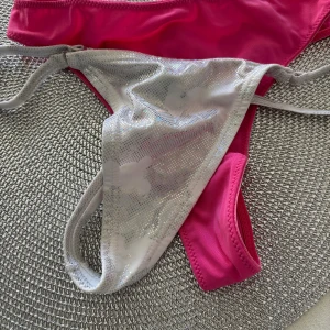 Glittrig stringtrosa i silver och en i rosa. - Säljer två olika trosor – en glittrig silverfärgad och en klassisk rosa är enkel och stilren. Perfekt för dig som vill ha fina underkläder.