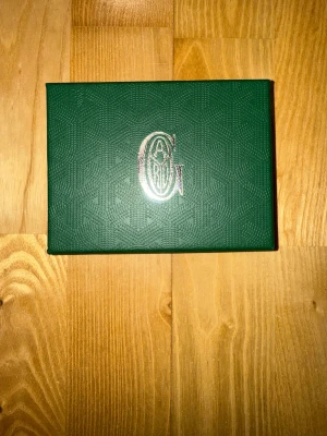 Korthållare  - En grön plånbok utstrålar både exklusivitet och karaktär. Den djupa, livfulla gröna tonen lyfter fram det ikoniska handmålade mönstret och gör varje plånbok unik. Lätt, slitstark och smart organiserad är den lika praktisk som den är lyxig. Ett perfekt val för dig som vill kombinera stil, hantverk och personlighet i ett enda elegant accessoarstatement.