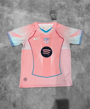 Rosa FC Barcelona Nike fotbollströja - Säljer en unik FC Barcelona fotbollströja från Nike i rosa med ljusblå och lila detaljer på ärmarna. Tröjan har korta ärmar, V-ringad krage med blå kant, och coolt grafiskt mönster framtill. Materialet är lätt och andas, perfekt för match eller träning. Spotify-logga och FCB-emblem på bröstet.