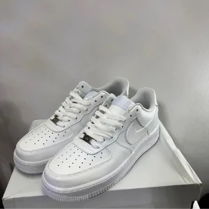 Nike Air Force 1  - Nike Air Force 1 Low sneakers i helvitt med klassisk rund tå och platt sula. Skorna har snörning, perforerad tåbox och tydlig Nike Swoosh på sidorna. Tillverkade i skinn med vit textilfoder och metallplatta på snörningen. Perfekt för dig som gillar clean och stilren look. Ena snöret har lite difekter 