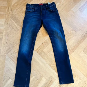 Mörkblå slim jeans från Jack & Jones - Snygga mörkblå jeans från Jack & Jones med klassisk femficksdesign och diskreta slitningar. Jeansen har slimmade ben och normal passform, tillverkade i mjukt denimtyg med lite stretch för extra komfort. Perfekta för en avslappnad och stilren look. Hör av er vid frågor