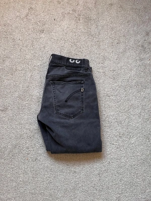 Gråa dondups - Säljer ett par grå jeans från dondup med snygga slitningar och coola detaljer på bakfickorna. Jeansen har en tapered passform som sitter skönt och ger en modern look. Klassisk femficksmodell med dragkedja och knapp framtill.