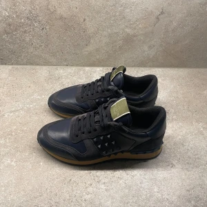 Valentino Rockrunner sneakers i marinblå  - Säljer nu dessa grymt snygga skor från Valentino! Modell: Rockrunner. Nypris ca 7500kr, mitt pris endast 2099. Skick 8,5/10 (se bilder), inget og medföljer vid köp. Storlek 41,5 – sitter ungefär 1-0,5 storlek större. Hör av er vid funderingar!