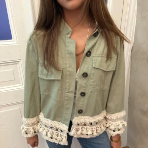 Grön jeansjacka med detaljer  - ‼️Säljer fler på min profil‼️Snygg ljusgrön overshirt med stora svarta knappar och två bröstfickor. Jackan har unika virkade detaljer med tofsar och pärlor längs nederkant och ärmslut, vilket ger en boho-vibe. Perfekt att slänga över en t-shirt för en chill look.