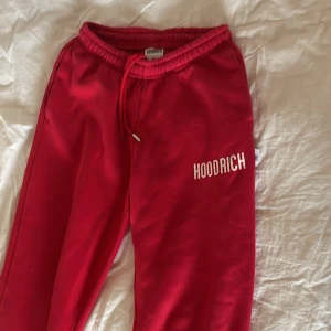 Röda Hoodrich mjukisbyxor XS - Snygga röda mjukisbyxor från Hoodrich i storlek XS. Byxorna har elastisk midja med snörning och resår vid bensluten. Hoodrich-loggan är tryckt i vitt på benet. En av detaljerna på byxknytet saknas 