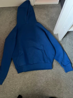 Blå oversized hoodie från FSBN - Säljer en blå hoodie från FSBN i oversized fit, storlek XS. Tröjan har huva, lång ärm och en stor magficka framtill. Materialet är mjuk bomull och passformen är loose, perfekt för en chill och avslappnad stil.