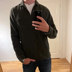 Mörkgrön overshirt från Dobber - Snygg mörkgrön overshirt från Dobber i storlek medium. Skjortan har klassisk krage, knappstängning framtill och en bröstficka med knapp. Materialet är mjukt och känns som bomull, perfekt att ha över en t-shirt för en chill look.