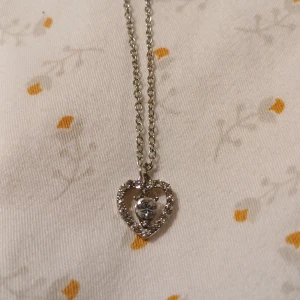 Silver Halsband Med Glittrande Hjärta Kristall - Jättegulligt Silver Halsband med Glittrande Kristallhjärta. Kedjan är relativt kort, perfekt längd enligt mig, inte för lång eller för kort. Sparsamt använd. Mycket gott skick. 🌷