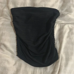 Tub topp från gina tricot - Säljer en svart tight kortkjol med snygg drapering på sidorna. Kjolen har en enkel och stilren design, perfekt för dig som gillar minimalistiska plagg med en twist. Materialet är mjukt och stretchigt för en bekväm passform.