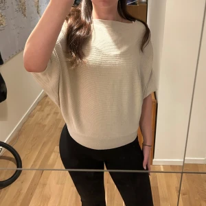 Beige ribbad bolerotopp med bred hals - Säljer en beige bolerotopp med bred hals och ribbad struktur. Toppen har en loose passform med korta, vida ärmar och sitter snyggt över axlarna. Perfekt att styla med svarta jeans eller kjol för en chill och trendig look.