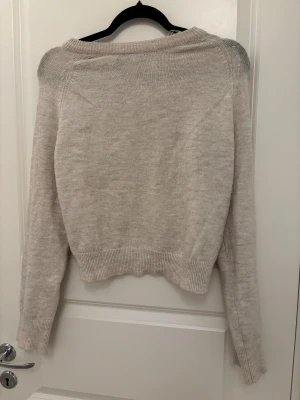 Beige stickad tröja från Divided - Mysig beige stickad tröja från Divided i storlek XXS. Tröjan har ribbade muddar vid hals, ärmslut och nederkant samt långärmad passform. Perfekt för lager-på-lager och chill stil.