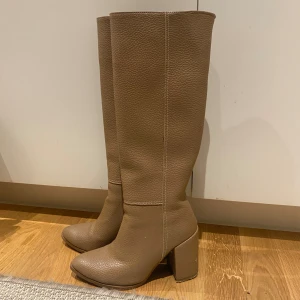 Beiga höga stövlar med klack - Pris kan diskuteras!!❤️❤️ Snygga höga stövlar i beige skinn med grov struktur och markerade sömmar. Modellen har en rejäl blockklack och spetsig tå, vilket ger en trendig siluett. Perfekta att styla med kjol eller jeans för en cool look. Skriv för frågor!