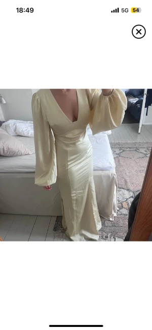 Champagnefärgad långklänning med v-ringning - Snygg långklänning i champagnefärg med djup v-ringning och vida, långa ärmar från Adoore. Klänningen har en figurnära passform och är tillverkad i ett glansigt material som ger en lyxig känsla. (Bilderna är lånade då jag inte får på mig min) Alla prislappar sitter kvar och är helt oanvänd💕