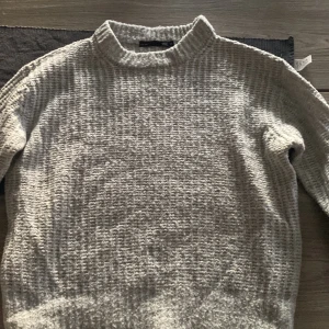 Grå stickad tröja från 157 XS - Säljer en grå stickad tröja från 157 i storlek XS. Tröjan har en högre krage och ett grovt, ribbat mönster som ger en cool och mysig vibe. Perfekt för dig som gillar enkel och stilren design med lite struktur.