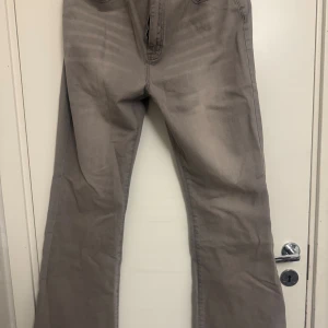 Grå bootcut jeans med hög midja - Snygga grå jeans med bootcut-ben och hög midja. Klassisk femficksmodell med dragkedja och knapp framtill. Jeansen har en mjuk tvättad look och är tillverkade i ett stretchigt bomullsmaterial för skön passform.