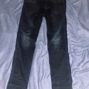 Replay Anbass mörkblå jeans, storlek 33 - Mörkblå Replay Anbass jeans med snyggt tvättad look och klassiska fem fickor. Slimmad passform och raka ben, med Replay-logga på bakfickan och läderpatch i midjan. Jeansen är tillverkade i stretchigt bomullsmaterial för extra komfort.