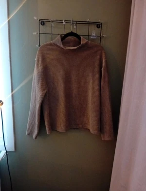 Olivgrön ribbad polotröja - Säljer en olivgrön polotröja med ribbad struktur och lång ärm. Tröjan har en lös passform och är tillverkad i mjukt material som känns skönt mot huden. Perfekt för dig som gillar enkel och stilren design med lite extra textur.